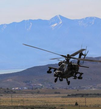 Helicóptero AH-64 Apache del Ejército de EE. UU. en vuelo sobre terreno montañoso.
